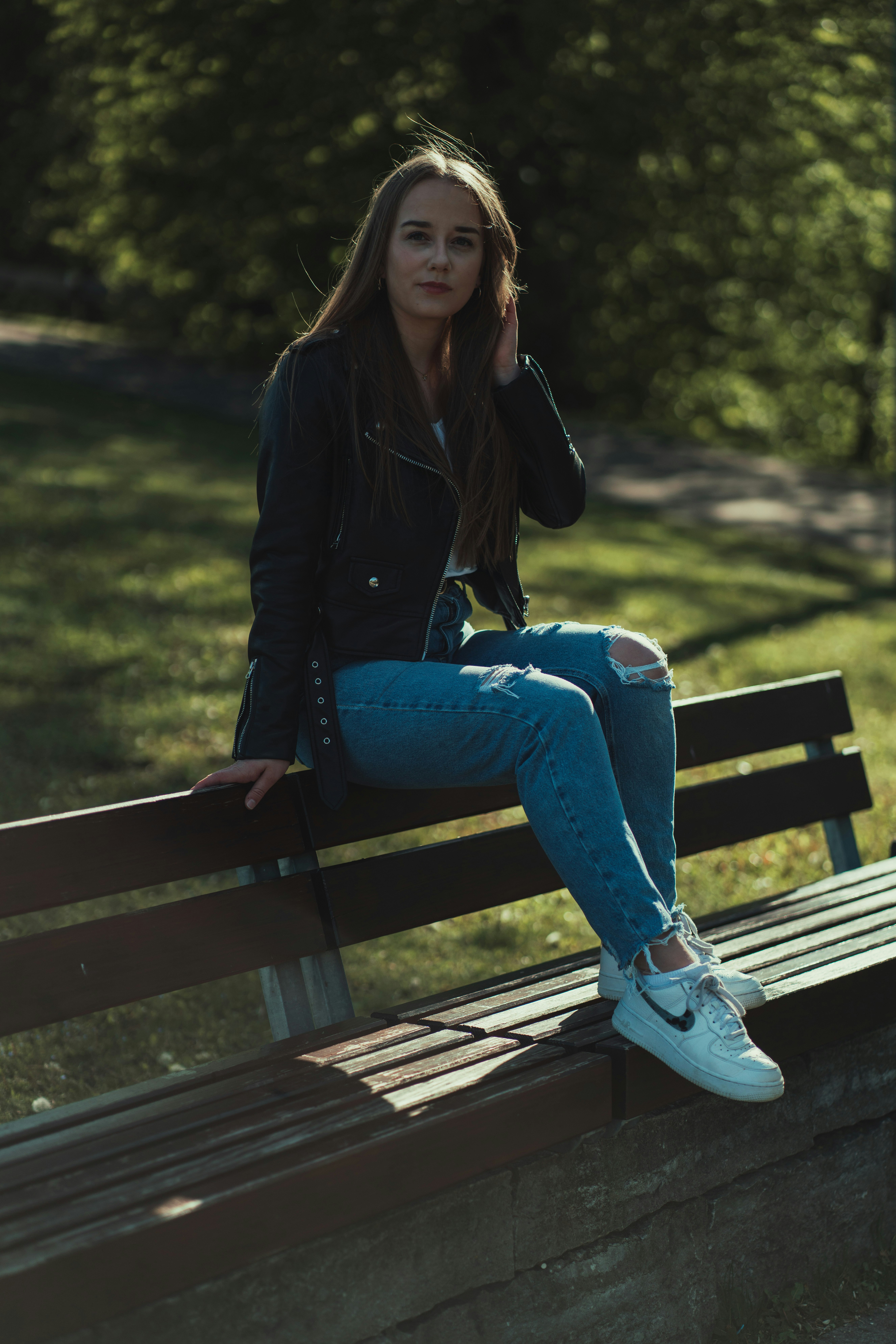 woman in black jacket and blue denim jeans sitting on brown wooden bench
